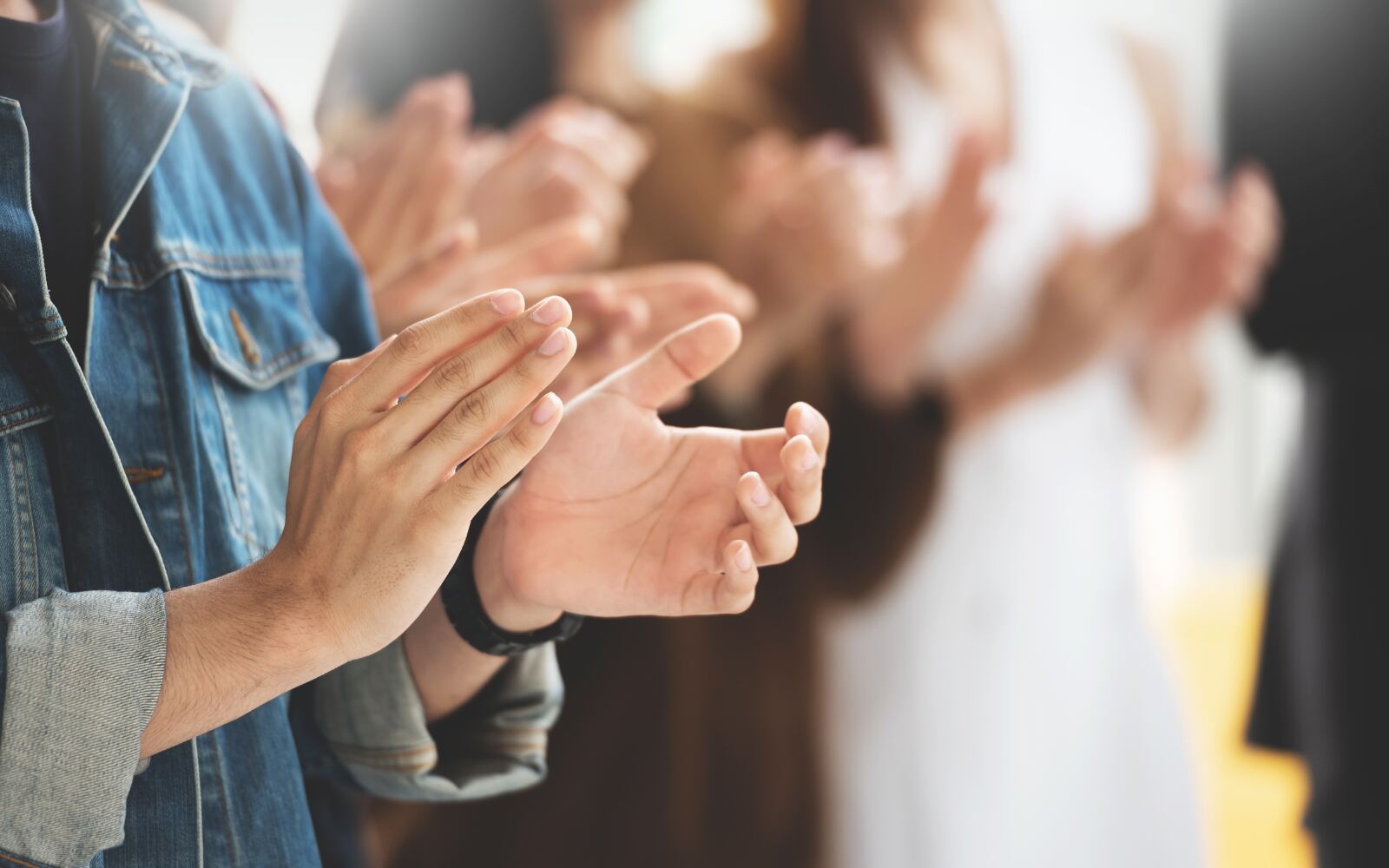 a close up shot of hands clapping, with other people clapping in the background, blurred out.  It gives the feeling of a crowd celebrating.