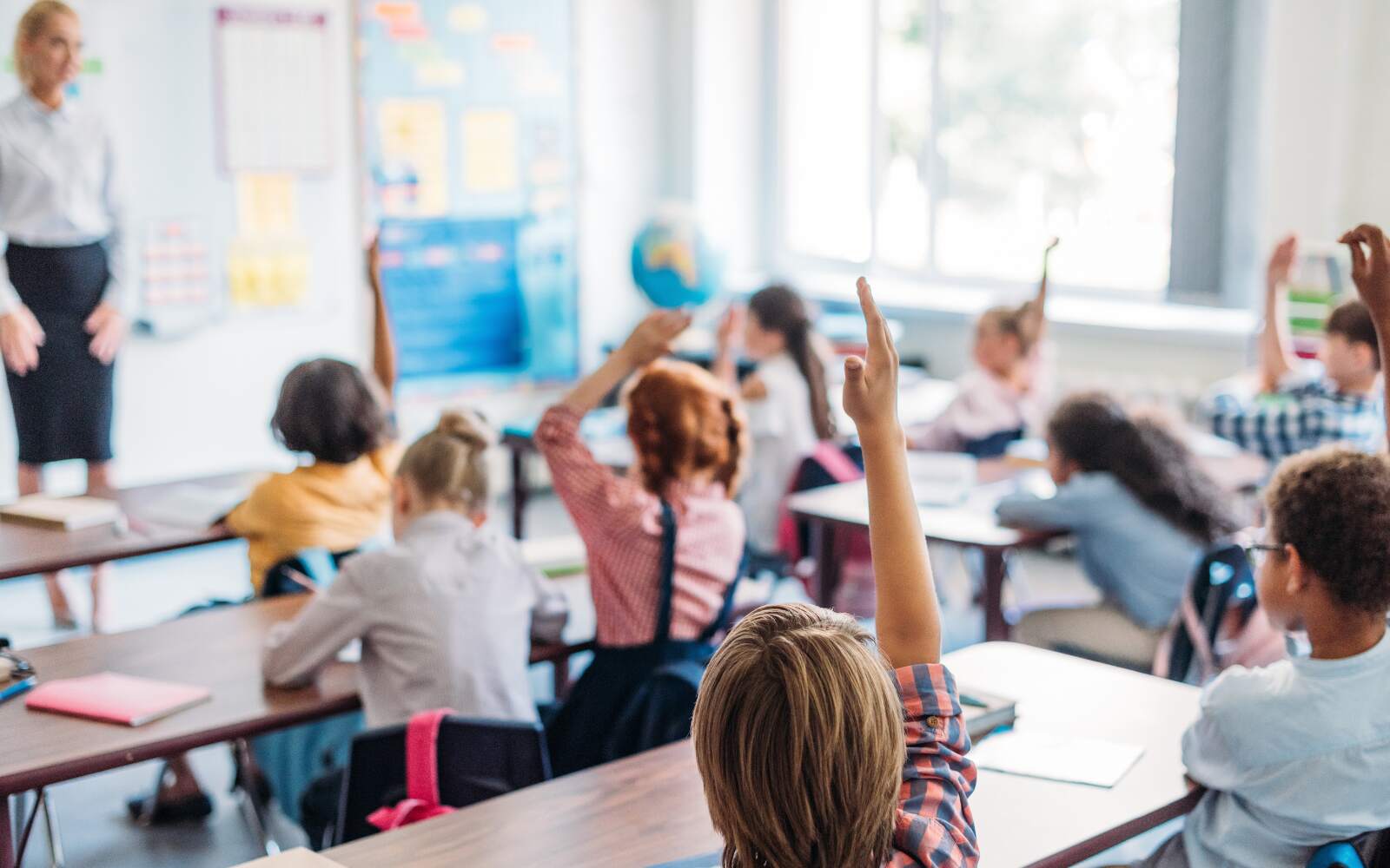 kids during lesson in classroom, image is taken from behind them with the teacher out of focus