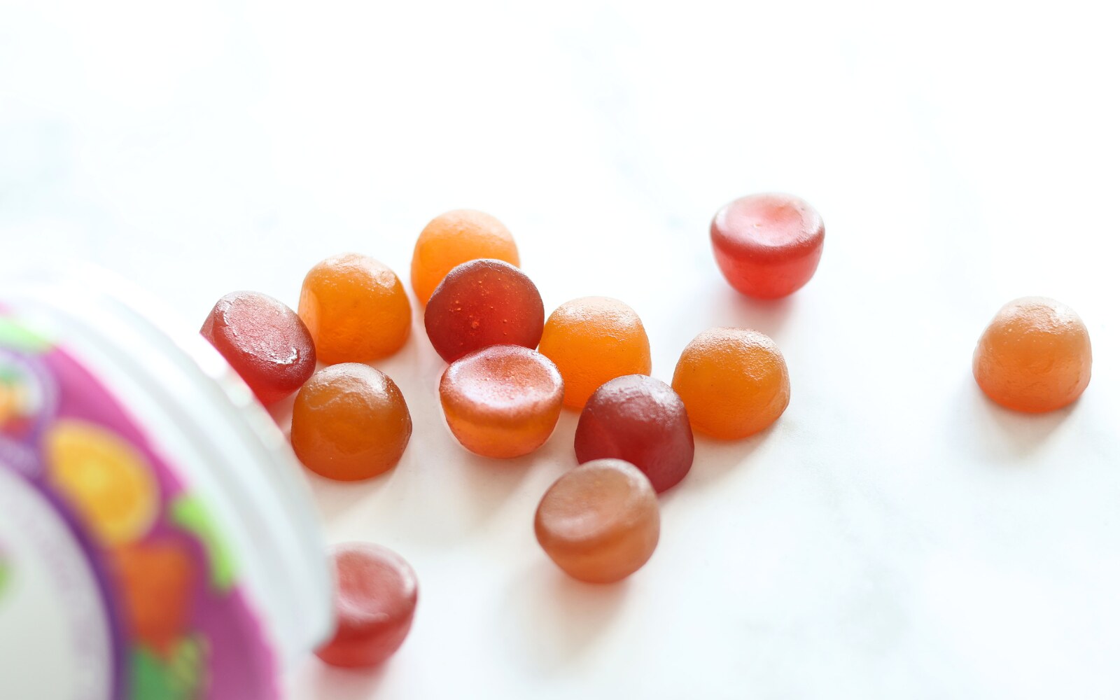 A bright image of Nutramin vitamin gummies spilled over onto a white background.  The sugar free gummies are cherry red, orange, and strawberry pink.