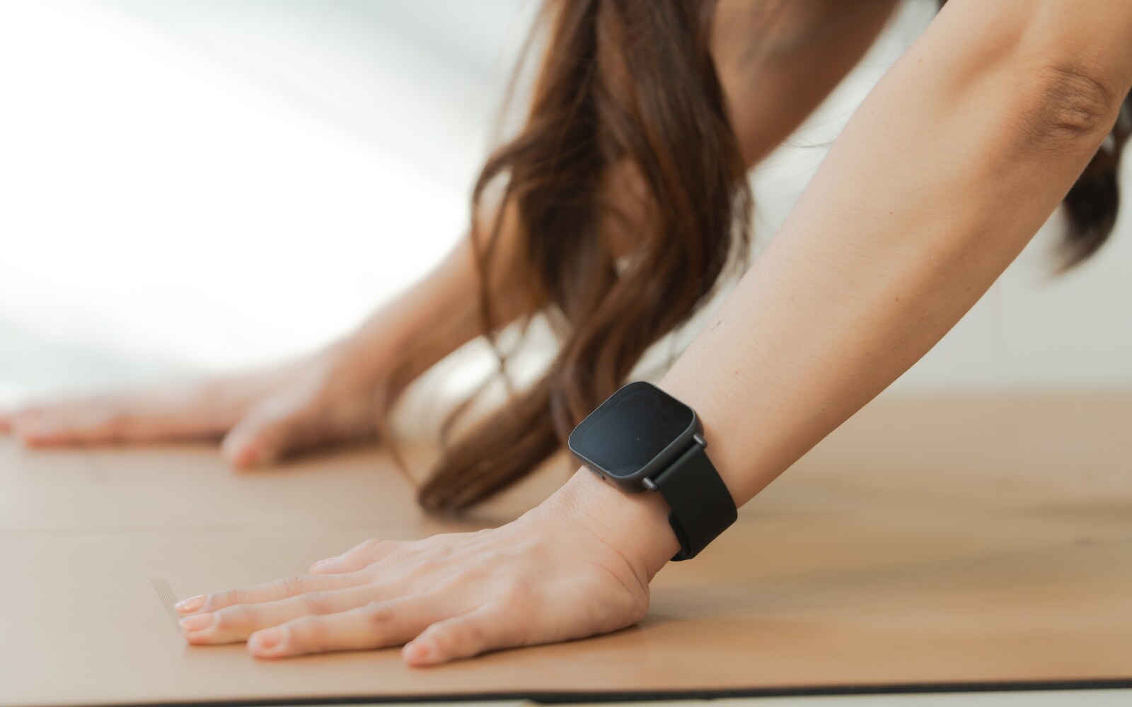 Woman exercising on wooden floor with smart watch, close up of arm and hand in yoga pose