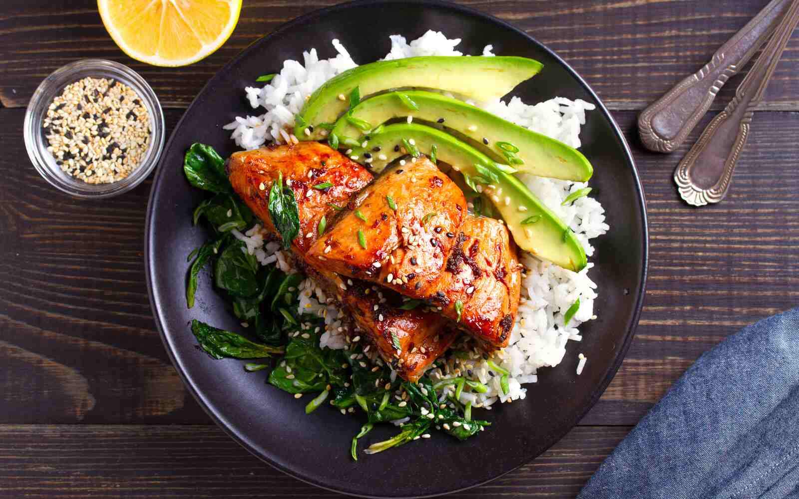 Salmon teriyaki rice bowl with spinach and avocado. View from above, on a dark brown table.